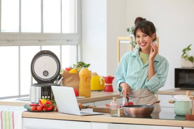 Dizüstü bilgisayarlı güzel bir kadın mutfakta dolma biber kesiyor.