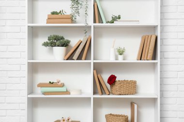 Beyaz tuğla duvarın yanında çiçekler ve bitkilerle dolu bir kitaplık.