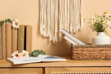 Bej duvarın yanındaki çekmecelerde çiçekler olan kitaplar.