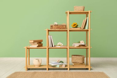 Odada yeşil duvarın yanında çiçekler olan kitaplık.