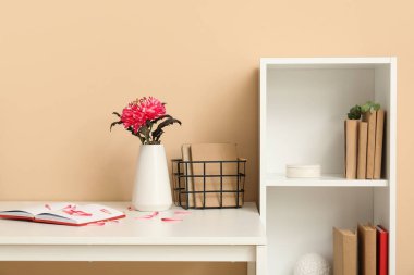 Bej duvarın yanında çiçek ve kitaplık olan işyeri