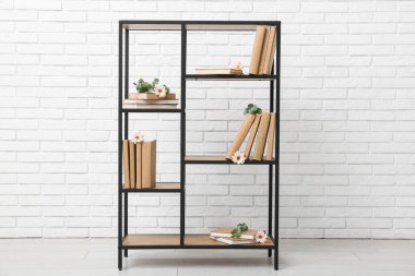 Odada beyaz tuğla duvarın yanında okaliptüs çiçekleri olan bir kitaplık.