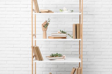 Beyaz tuğla duvarın yanında çiçek ve okaliptüs olan bir kitaplık.