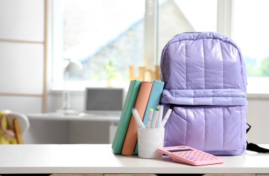 Kalem fincanı, hesap makinesi ve kitaplarla dolu eflatun sırt çantası.