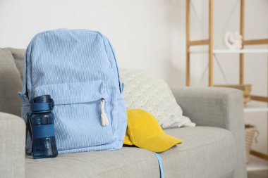 Oturma odasındaki kanepede su şişesi ve şapkalı mavi sırt çantası.