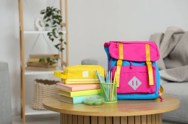 Oturma odasındaki masada kırtasiye malzemesi ve kitaplarla dolu sırt çantası.