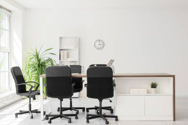 Masası, raf ünitesi ve palmiye bitkisi olan konferans salonunun içi.