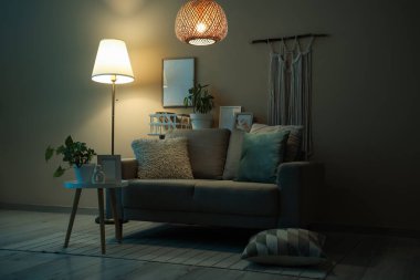 Geceleri parıldayan lambaları, kanepesi ve masaları olan karanlık oturma odasının içinde.