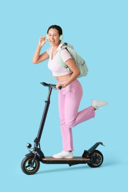 Mavi arka planda elektrikli scooter kullanan kulaklıklı Afro-Amerikan bir kız öğrenci.