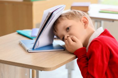 Kitapçığı olan küçük bir öğrenci sınıfta masa başında tırnak yiyor.