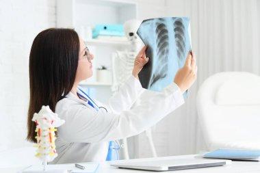 Kadın doktor klinikteki masada akciğerlerin röntgen görüntülerini inceliyor.