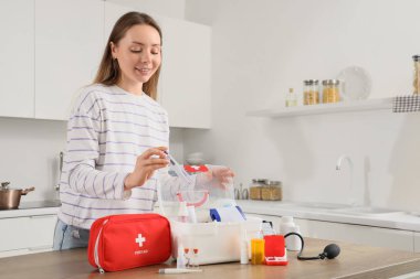 Mutfaktaki ilk yardım çantalarından termometre alan genç bir kadın.