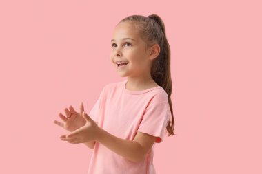 Sevimli küçük kız pembe arka planda el çırpıyor.