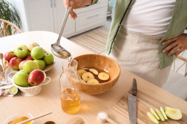 Olgun bir adam mutfaktaki masada cam şişeye elma şarabı dolduruyor.