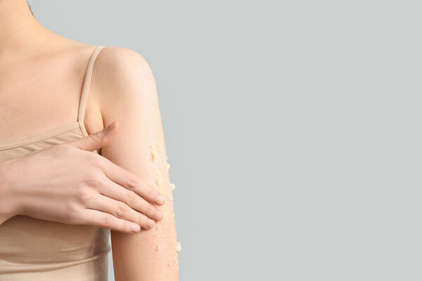 Молодая женщина нанесла естественный скраб на плечо на сером фоне, крупным планом