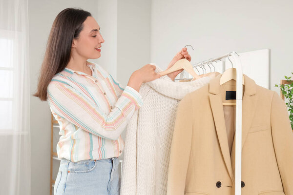 Молодая женщина собирает одежду со стойки в спальне