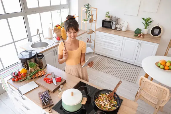 Mutfakta tablet bilgisayarı olan genç bir kadın.