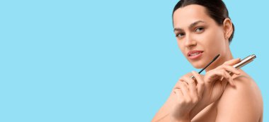 Açık mavi arkaplanda rimel tutan genç ve güzel bir kadın.