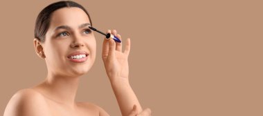 Güzel genç bir kadın kahverengi arkaplan üzerine rimel sürerken mesaj için boşluk bırakıyor.