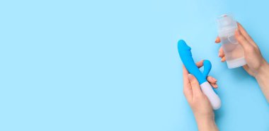 Kadının elleri mavi arka planda tavşan vibratörü ve bir şişe kayganlaştırıcı tutuyor.