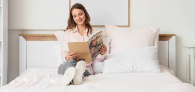 Yatakta dergi okuyan güzel bir genç kadın. 