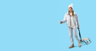 Kış kıyafetleri içinde mutlu genç bir kadın ve mavi arka planda kızağıyla mesajlaşmak için yeri var.