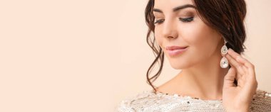 Bej arka planda şık mücevherler takan güzel bir genç kadın.