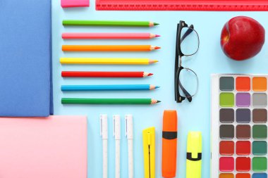 Taze kırmızı elmalı gözlük ve mavi arka planda farklı kırtasiye malzemeleri.