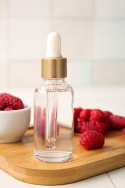 Beyaz fayans zemininde bir şişe kozmetik ahududu yağı olan ahşap tahta, yakın plan.