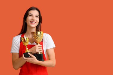 Turuncu arka planda altın bardakları olan kadın işçi.