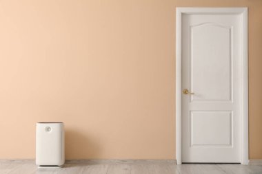 Odada bej duvarın yanında hava temizleyici var.