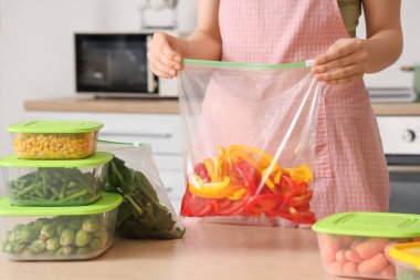 Ahşap masada donmak için elinde dolma biberle plastik poşet tutan kadın.