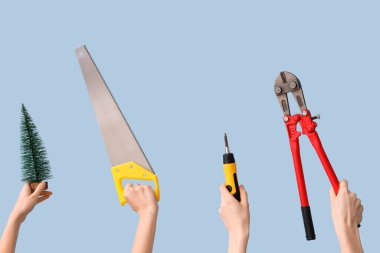 Açık mavi arka planda inşaat aletleri ve Noel süslemeleri tutan eller