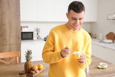 Genç adam mutfakta lezzetli yoğurt yiyor.