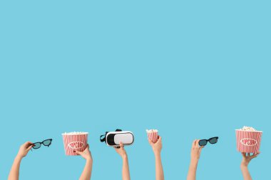 Mavi zemin üzerinde patlamış mısır, VR kulaklık ve 3D gözlük bulunan kovaları tutan eller.