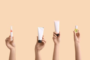 Bej arka planda kozmetik krem tüpleri ve tırnak yağı olan kadın elleri.