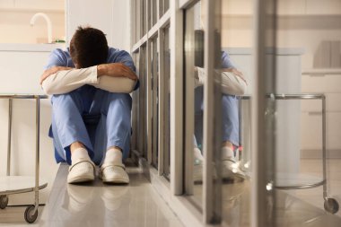 Stressed male nurse sitting on windowsill at hospital in evening