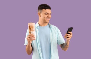 Lezzetli bir donör kebabı ve eflatun arka planda cep telefonu olan yakışıklı bir genç.