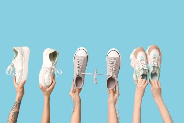 Mavi arka planda farklı şık spor ayakkabıları olan kadın elleri.