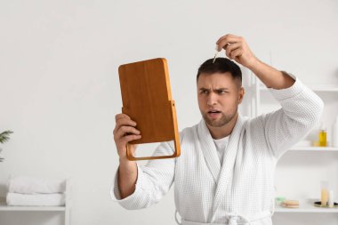 Aynalı genç adam banyoda saç uzatmak için serum kullanıyor.