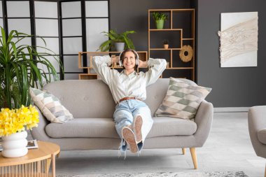 Kulaklıklı güzel bir kadın evdeki kanepede müzik dinliyor.