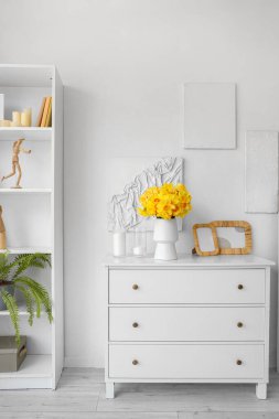 Oturma odasında nergis, mum ve çerçeveli vazo.