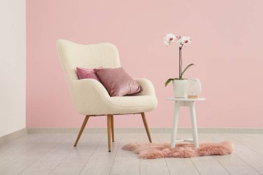 Yastıklı beyaz koltuk, orkideli kahve masası ve pembe duvarlı yumuşak halı.