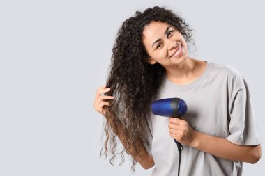 Güzel, genç, mutlu, Afro-Amerikan bir kadın. Sağlıklı kıvırcık saçlarını gri arka planda kurutuyor.