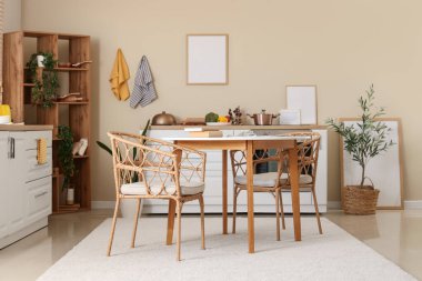 Modern mutfak, yemek masası, beyaz tezgahlar ve bej duvarda asılı boş çerçeveler.