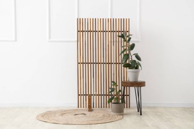 Beyaz duvarın yanında ahşap perdeli, masalı ve çiçekli bir oda.