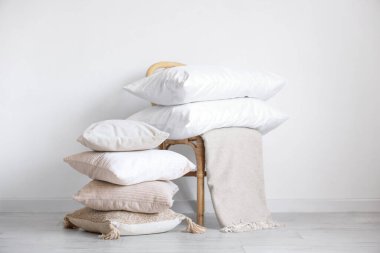 Beyaz duvarın yanında yastık desteleri olan hasır sandalye.