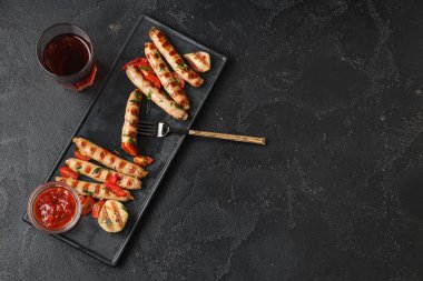 Lezzetli ızgara sosis, bir kase sos ve siyah arka planda bir bardak bira.