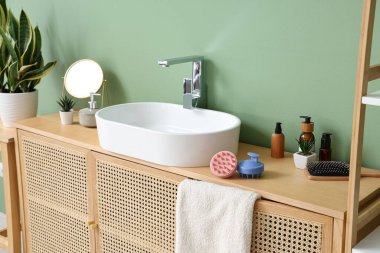 Yeşil duvarın yanındaki çekmecelerde banyo aksesuarlarıyla lavabo.