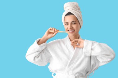 Bornozlu, mavi arka planda diş fırçası olan güzel, genç ve mutlu bir kadın.
